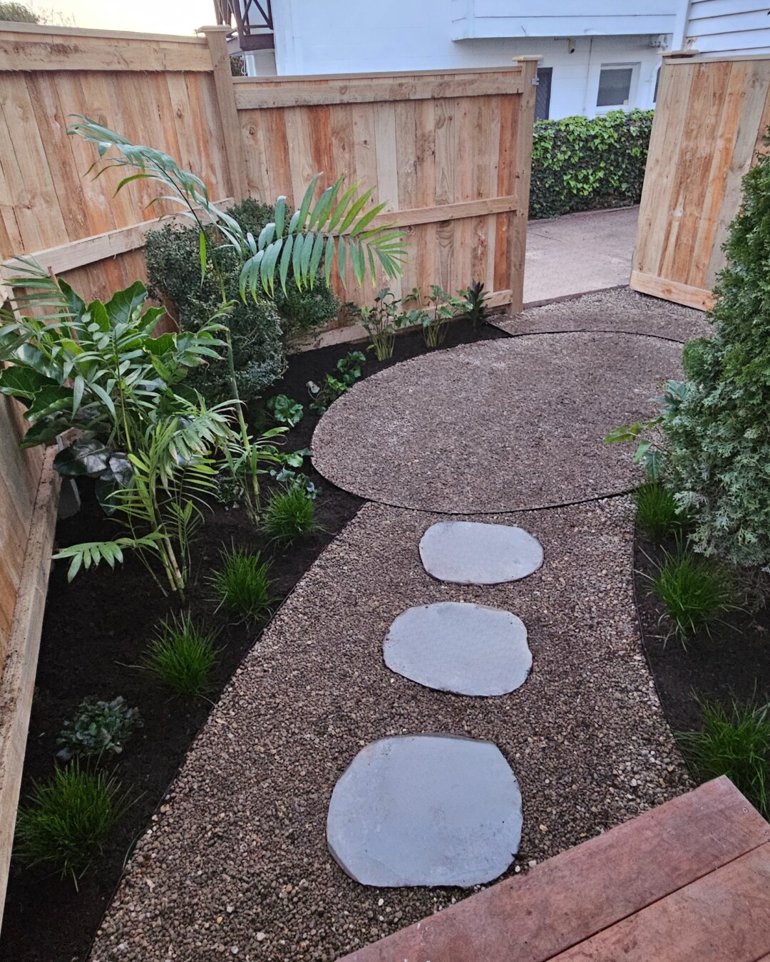 Curved decorative gravel garden path with large stepping stones, fresh planting and timber fencing